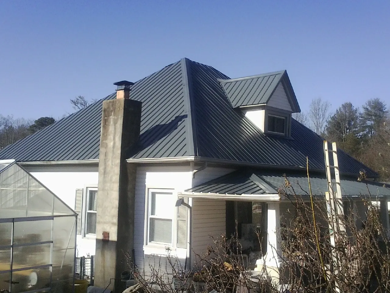 Dark blue standing seam metal roof on a white farmhouse with dormer — Slate & Tile Roof Repair by Roofing Brothers in South Barre