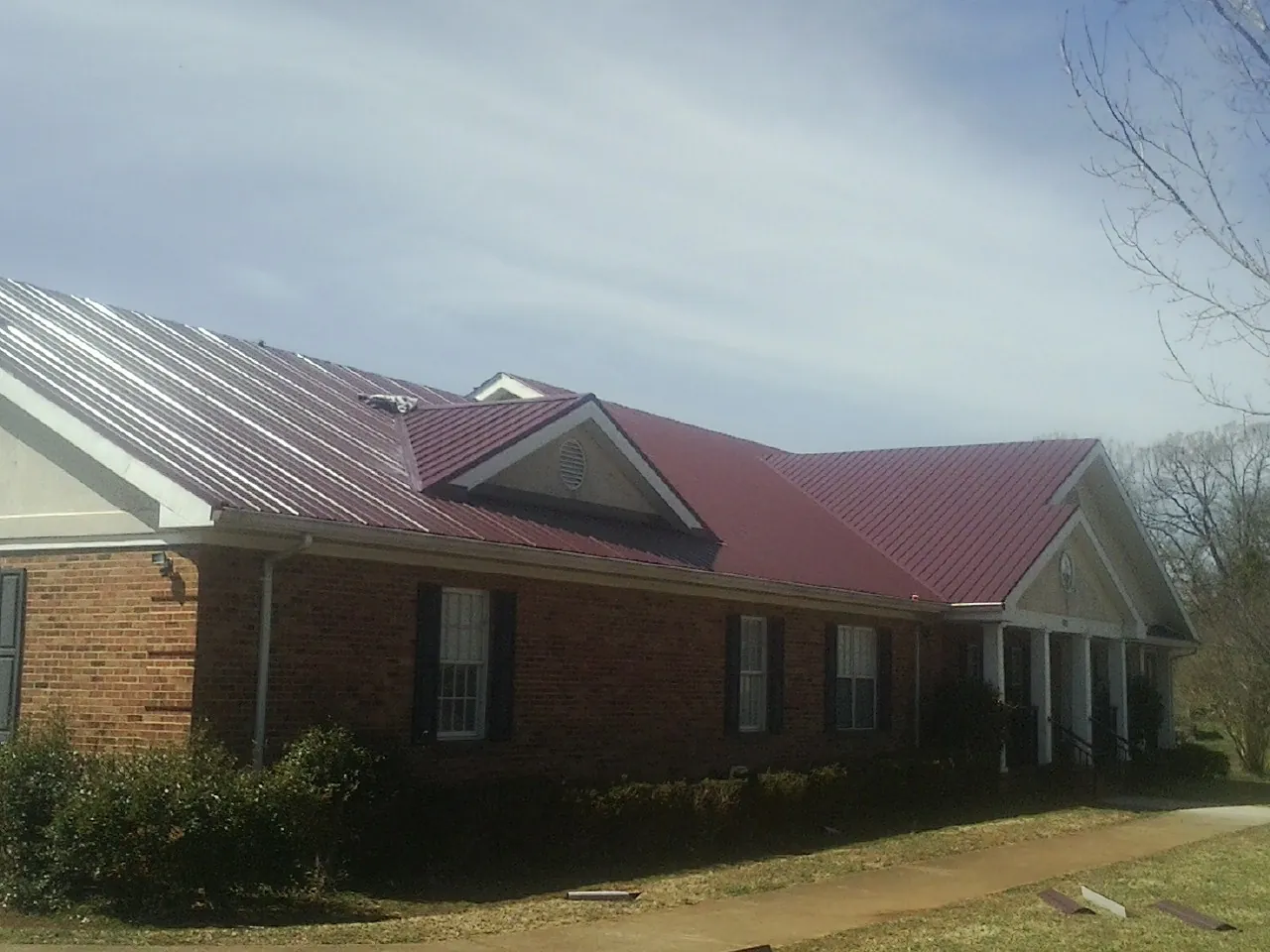 Red metal roof with gabled entries on a long brick building, from a Hail Damage Roof Repair job in South Barre