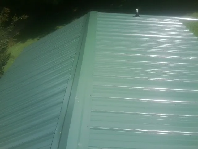 New green metal panels meeting at the ridge of a roof — Flat Roof Repair work by our crew in South Barre