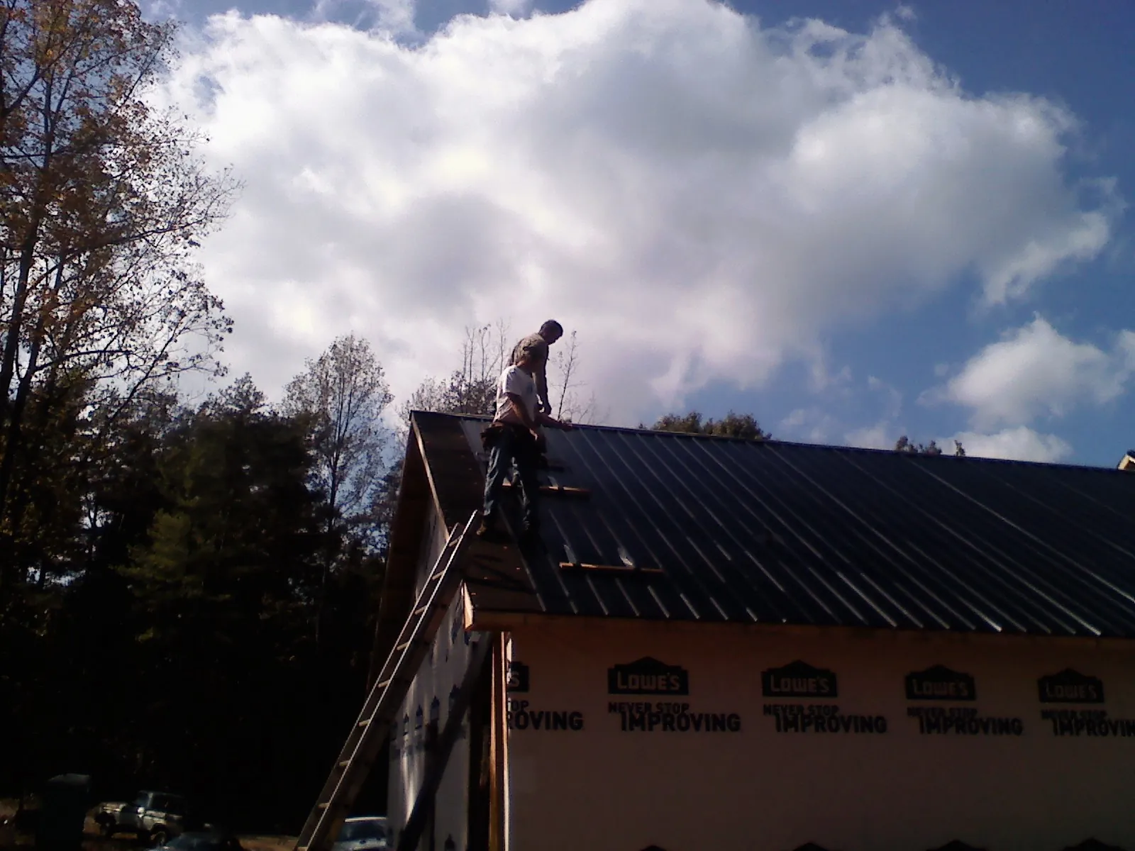 Roofer fastening dark metal panels high against a cloudy sky, from a Roof Inspection job in South Barre