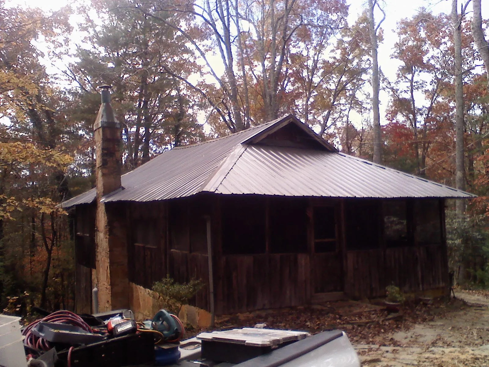 Brown metal hip roof on an old cabin with a stone chimney in South Barre