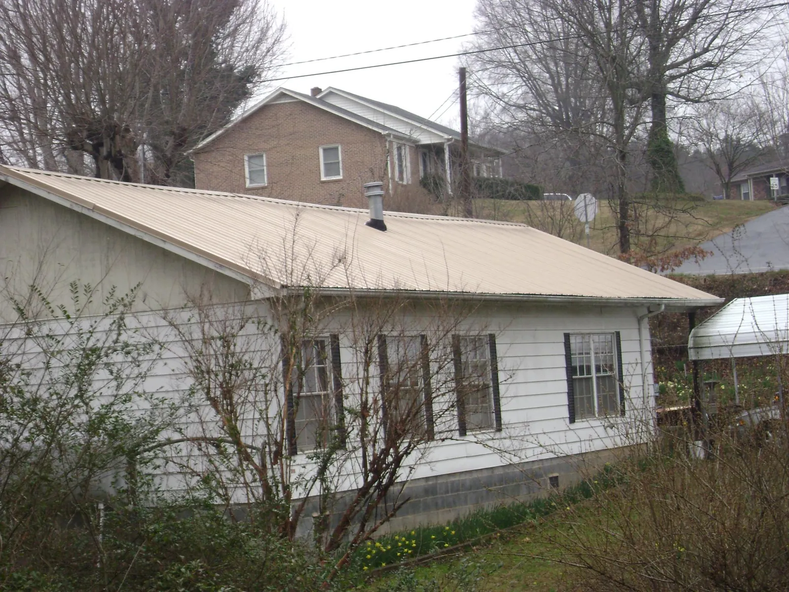 Tan metal roof on a white sided house set into a hillside — Commercial Roofing by Roofing Brothers in South Barre